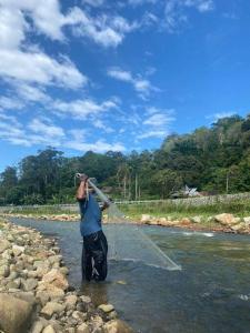 un hombre parado en un río sosteniendo una tubería en Homestay Hulu Langat with POOL and RIVER Free Fishing Village Panorama WiFi and Netflix en Hulu Langat