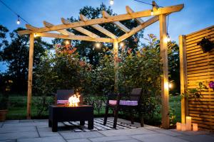 a wooden pergola with two chairs and a table with a fire at The Huts At Woodthorpes in Assington