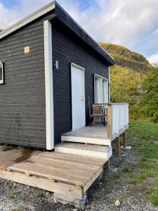 ein schwarzes winziges Haus mit einer Holzterrasse in der Unterkunft Overnatting med sjøutsikt å rolige omgivelser in Alta