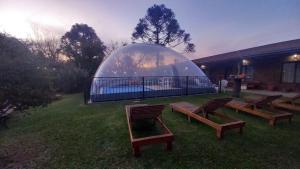 un groupe de bancs dans un champ avec un dôme de verre dans l'établissement Tierra Mansa - Posada de Campo & Spa - Piscina Climatizada, à Marcos Paz