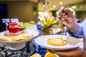 a person holding a plate of food with a fork and knife at WL Hotel Maputo City Center Mozambique Collection in Maputo