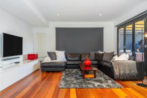 uma sala de estar com um sofá de couro preto e uma televisão em Elegant Port Melbourne Home Mins to Cafes and Beach by Custom Bnb Hosting em Melbourne