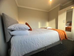 um quarto com uma cama com lençóis brancos e um cobertor laranja em The Coral Guest House 1 Fratton Park Portsmouth em Portsmouth