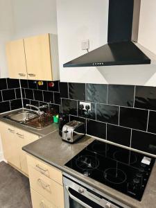 Il comprend une cuisine dotée de murs en carrelage noir et d'un four avec plaques de cuisson. dans l'établissement Bespoke 2 Bedroom Apt Derby City, à Derby