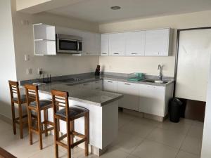 曼萨尼约HERMOSO DEPARTAMENTO DE LUJO EN MANZANILLO A PIE DE PLAYA EN PONTO HORIZONTE MANZANILLO. PARA HASTA 8 PERSONAS, DE LO MEJOR DE MANZANILLO. HERMOSA VISTA AL MAR的厨房配有白色橱柜和带吧台凳的台面 更多11张照片