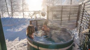 duas pessoas numa banheira de hidromassagem na neve em Lysti Cottage by the lake and magical countryside em Rovaniemi