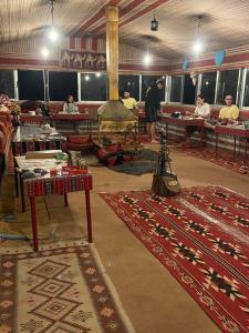 una habitación con alfombras y mesas y personas sentadas en mesas en Omar Ghazi Camp en Wadi Rum