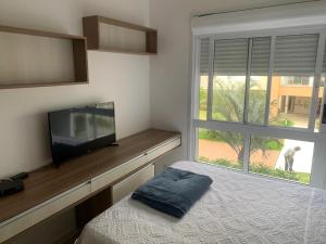 1 dormitorio con 1 cama, TV y ventana en Apartamento na Praia do Campeche, en Florianópolis