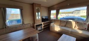 a living room with a couch and a tv and windows at NB166 - Porth Bay Hideaway in Porth