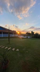 una puesta de sol en un campo con un edificio al fondo en Chácara Recanto dos Pássaros, en São Thomé das Letras