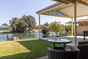 un patio con mesa y sillas junto a una masa de agua en Seabreeze on Ibis, en Sussex Inlet