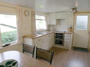 a kitchen with white cabinets and a table and chairs at Brightwater Cottage in Arnisdale