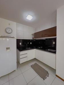 a kitchen with white cabinets and a clock on the wall at Apê Laranja Iloa Barra de São Miguel in Barra de São Miguel