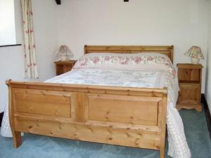 a bedroom with a wooden bed and two night stands at The Stables Trap Farm in Wolves Newton