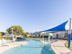 einen Pool mit Stühlen und Sonnenschirmen neben einem Gebäude in der Unterkunft NRMA Warrnambool Riverside Holiday Park in Warrnambool