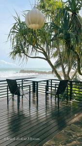 a table and two chairs on a boardwalk next to the beach at Elysium in Unawatuna
