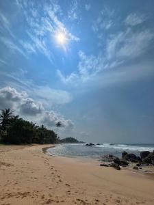 a beach with rocks and the sun in the sky at Elysium in Unawatuna