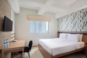 a bedroom with a white bed and a desk and a window at All Nite and Day Hotel Alam Sutera in Serpong