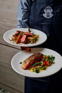 a person holding two plates of food with meat and vegetables at Rydges Geelong in Geelong