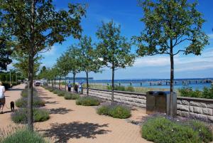 a sidewalk next to the water with trees and people walking a dog at Appartementhaus mit Balkon im Ostseebad Göhren HM-01-09 in Göhren
