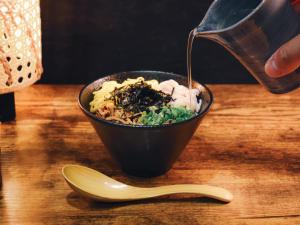 a person pouring sauce into a bowl of food at The BREAKFAST HOTEL Fukuoka Nakasu in Fukuoka