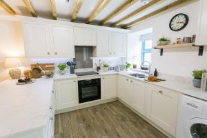 a kitchen with white cabinets and a clock on the wall at Ysgubor Wennol in Llanfairpwllgwyngyll