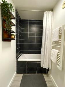 een badkuip in een badkamer met zwarte tegels bij Séjour Business & Famille, 2 chambres, Parking & WiFi in Brétigny-sur-Orge