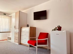 Habitación con silla roja y TV en la pared. en Studio Apartman Iovia place en Ludbreg