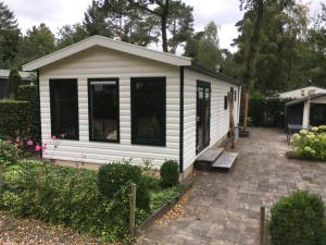 a small white shed with black windows and a patio at Forest Family 6 persoons op 5 sterren park in Beekbergen