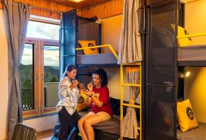 two women sitting on a bunk bed playing guitar at The Hosteller Chakrata in Chakrāta