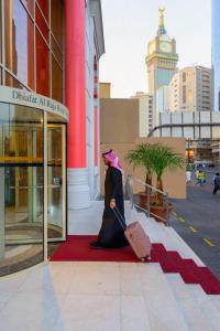 una mujer está de pie en una alfombra roja con una maleta en Dhiafat Al Raja Hotel, en La Meca