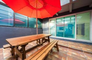 Hotel Lien في بوسان: مقعد خشبي مع مظلة حمراء أمام المبنى