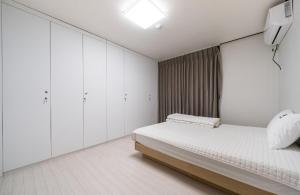 a white bedroom with a bed and white cabinets at Hotel Lien in Busan
