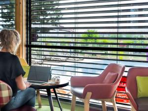 een vrouw aan een tafel met een laptop voor een raam bij Ibis Styles Colmar Nord in Colmar
