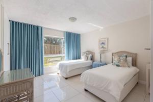 een slaapkamer met 2 bedden en een raam met blauwe gordijnen bij 7 Kenwyn On Sea in Ballito +12 foto's
