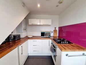 a kitchen with white cabinets and a purple accent wall at Bright top floor, 1 bed apartment in great location in London