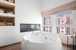 a white bathroom with a tub and a large window at Chic Studio with a Bath Tub, Pool & Gym near Golf Club in Dubai
