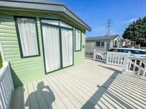 a green house with a wooden deck with a white fence at Lovely 6 Berth Caravan At Caldecott Hall Country Park, Norfolk Ref 91010c in Great Yarmouth