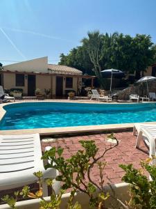 a swimming pool with two white chairs and a house at Hotel Grotticelli in Scopello