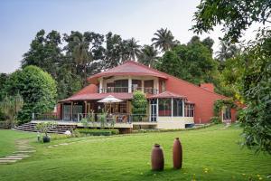 a red house on a green field with a yard at LohonoStays Villa Lani in Alibag