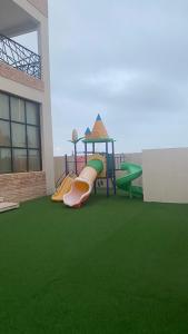 un parque infantil con tobogán en un edificio con césped verde en شالية مارينا مرباط, en Mirbāţ