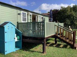a green house with a deck and a house at Muffins Meadow Shepherds Hut in Tillingham