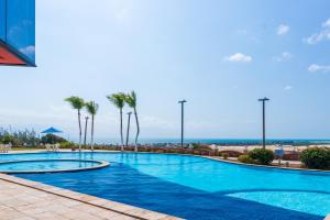 uma piscina com palmeiras e o oceano ao fundo em Porto d'Aldeia Hotel by Castelo Itaipava em Fortaleza