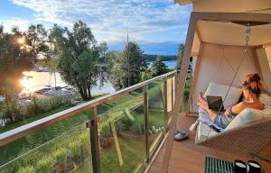 a woman sitting on a porch swing with a laptop at Marina Relax - widok na jezioro, parking podziemny, winda, Netflix, TV55" in Iława