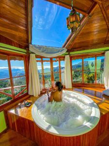 Una mujer en una bañera en una habitación con ventanas en Pousada Portal Dos Ventos, en Visconde De Maua