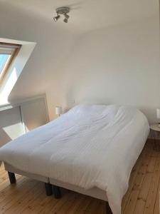 uma cama branca num quarto branco com uma janela em Maison au dessus de la plage em Saint-Michel-en-Grève