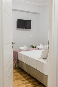 a white bedroom with a bed and a flat screen tv at The Little Pigeon - Pink in Ioannina