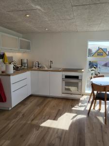 cocina con armarios blancos, mesa y ventana en Hyggelig lejlighed i Sandavágur, en Sandavágur