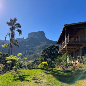 una casa en una colina con una palmera y una montaña en Casa Baúau en São Bento do Sapucaí