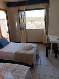 a bedroom with two beds and a desk and a window at Pousada A Pérola in Rio de Contas